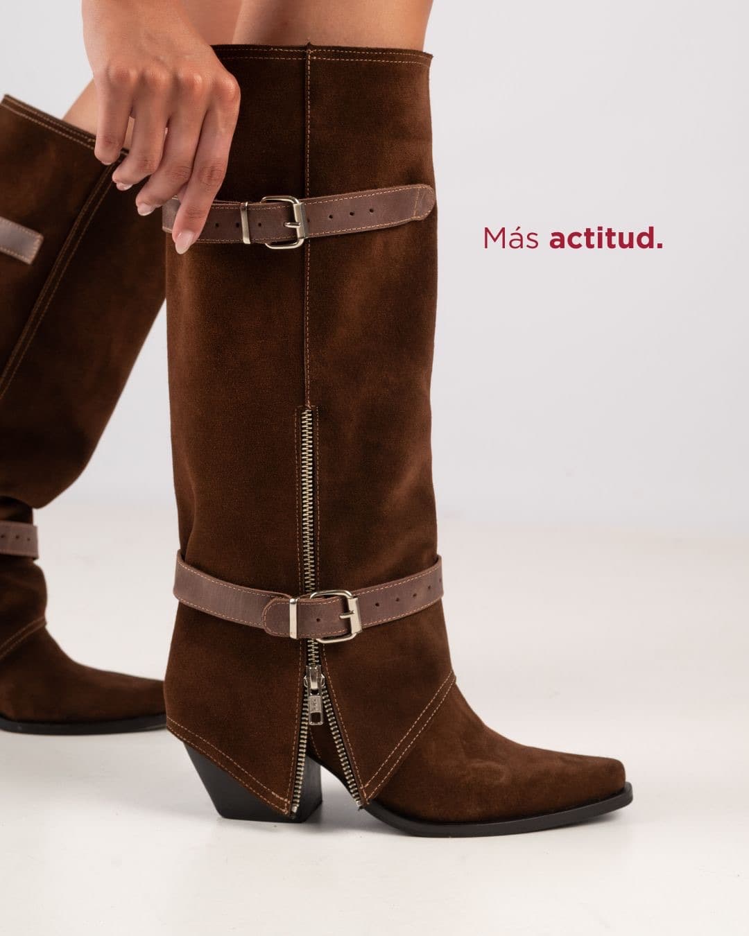 Cápsula Texanas: botas altas de gamuza marrón con hebillas y el texto «Más actitud»